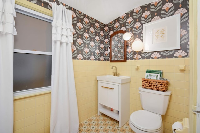 bathroom with toilet, a wainscoted wall, tile walls, vanity, and wallpapered walls