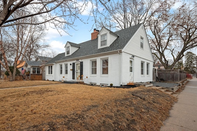 new england style home with a chimney, roof with shingles, fence, a front lawn, and brick siding