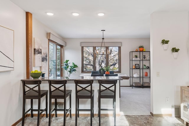 kitchen with baseboards, carpet floors, an inviting chandelier, a kitchen bar, and decorative light fixtures