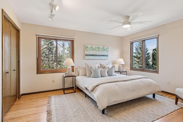 bedroom with a ceiling fan, baseboards, light wood finished floors, track lighting, and a closet