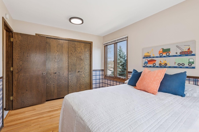 bedroom with a wainscoted wall, light wood-style flooring, and a closet