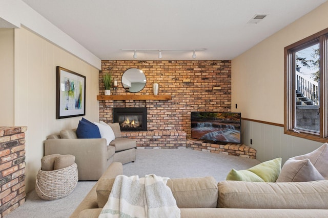 carpeted living area with visible vents, a wainscoted wall, track lighting, and a fireplace