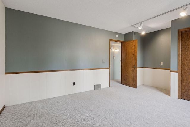 empty room with visible vents, carpet floors, wainscoting, and track lighting