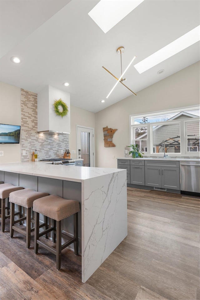 kitchen featuring tasteful backsplash, light stone countertops, a kitchen bar, a skylight, and stainless steel dishwasher