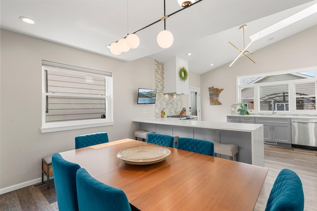 dining area featuring lofted ceiling with skylight, recessed lighting, baseboards, and wood finished floors