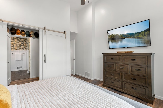 unfurnished bedroom featuring a barn door, baseboards, visible vents, and dark wood finished floors