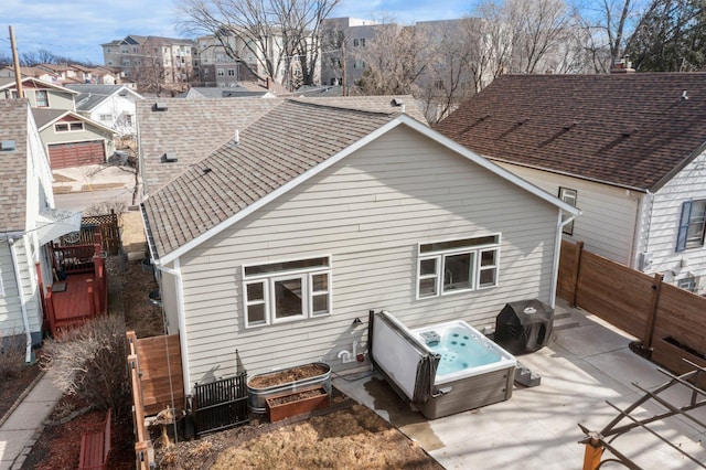 back of property with a fenced backyard, a hot tub, a shingled roof, and a patio