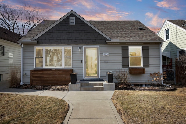 bungalow featuring a lawn and roof with shingles