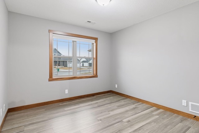 unfurnished room with light wood finished floors, baseboards, and visible vents