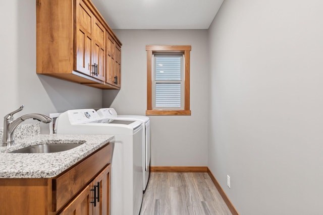 laundry area featuring cabinet space, light wood-style floors, a sink, independent washer and dryer, and baseboards