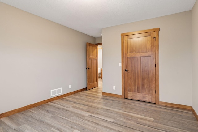 unfurnished bedroom with baseboards, a textured ceiling, visible vents, and wood finished floors