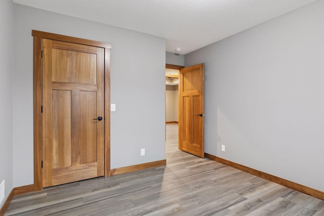 unfurnished bedroom with light wood-type flooring, baseboards, and a textured ceiling