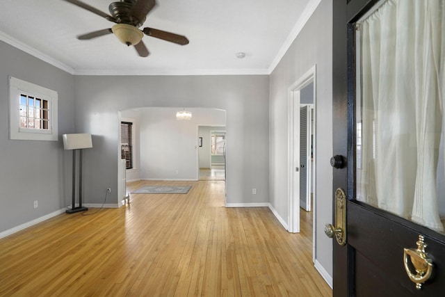 foyer with light wood-style flooring, ornamental molding, a ceiling fan, arched walkways, and baseboards