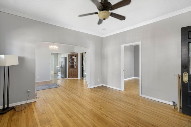 unfurnished living room featuring ornamental molding, arched walkways, light wood-type flooring, and baseboards