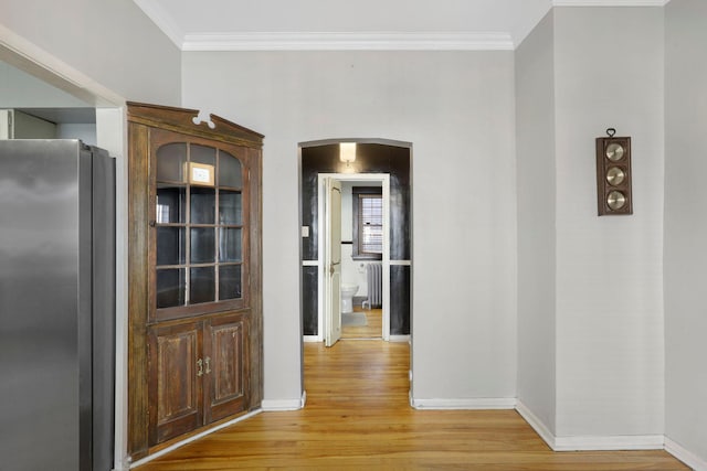 hall featuring baseboards, light wood-style floors, arched walkways, and ornamental molding