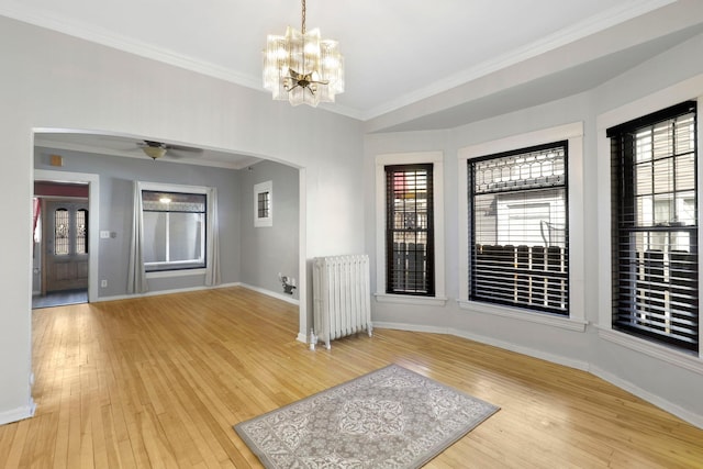 empty room featuring arched walkways, light wood finished floors, radiator, and baseboards