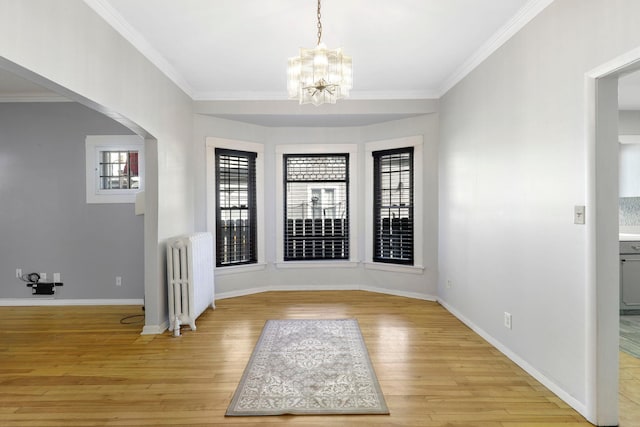 foyer entrance featuring light wood-style flooring, radiator heating unit, arched walkways, and ornamental molding