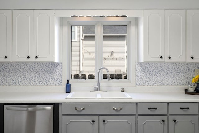 kitchen featuring a sink, light countertops, white cabinets, stainless steel dishwasher, and backsplash