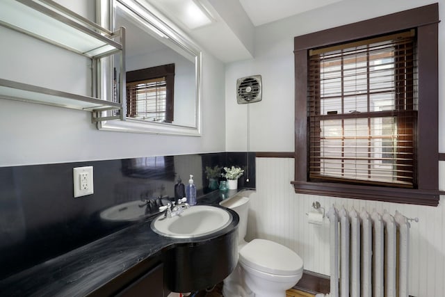 bathroom featuring toilet, radiator heating unit, vanity, and a wainscoted wall