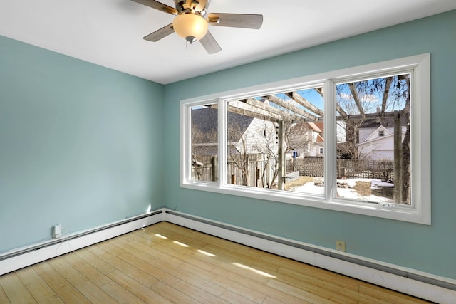 unfurnished room featuring baseboard heating, plenty of natural light, and wood finished floors