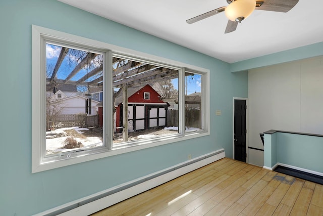 unfurnished dining area with a baseboard heating unit, wood finished floors, and a ceiling fan