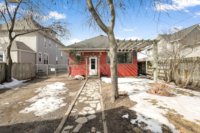 snow covered back of property with brick siding, a pergola, fence, and a gate