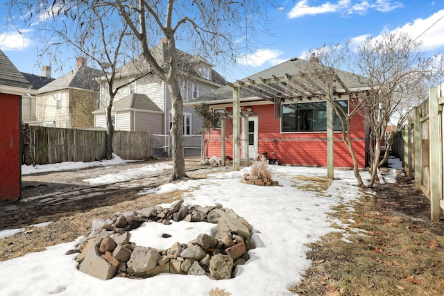 snow covered rear of property featuring a pergola and a fenced backyard