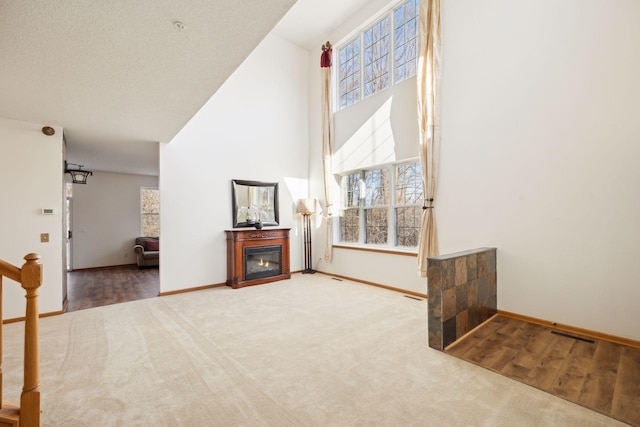 living area with a high ceiling, baseboards, carpet flooring, and a glass covered fireplace