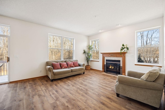 living area with a textured ceiling, a tiled fireplace, wood finished floors, and baseboards