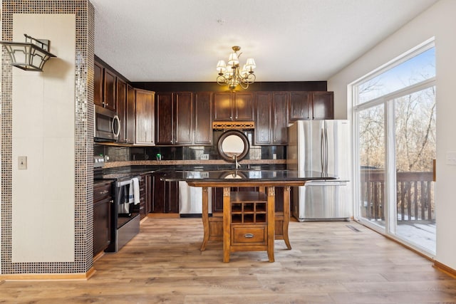 kitchen with light wood-style flooring, dark brown cabinetry, a notable chandelier, stainless steel appliances, and dark countertops