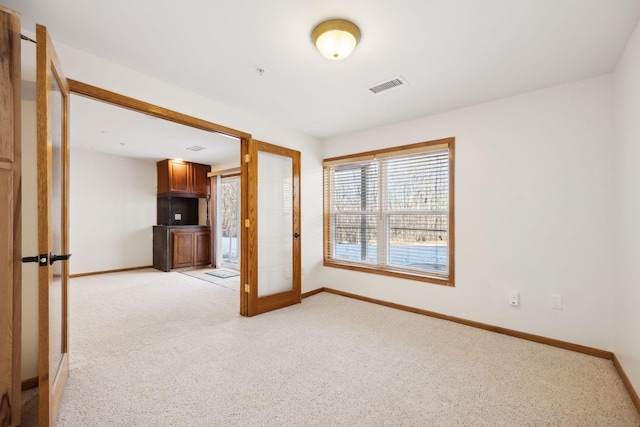 empty room with baseboards, visible vents, and light colored carpet