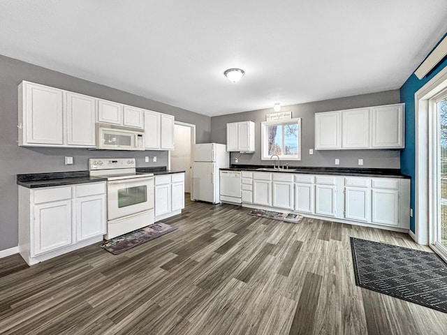 kitchen with dark countertops, white appliances, white cabinetry, and a sink