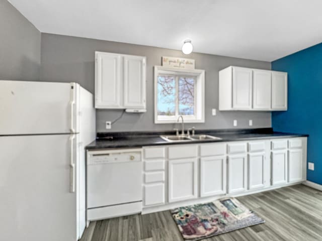 kitchen featuring dark countertops, white appliances, white cabinetry, and a sink