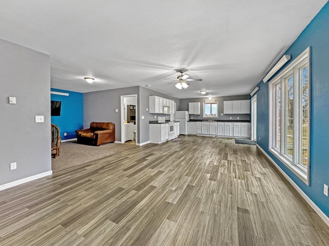 unfurnished living room with a sink, wood finished floors, a ceiling fan, and baseboards