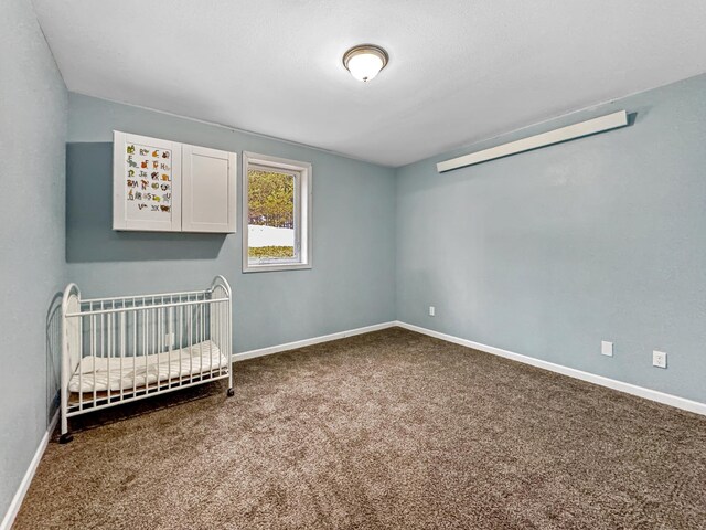 unfurnished bedroom featuring a nursery area, carpet, and baseboards