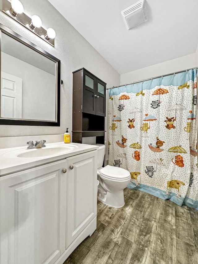 full bath featuring toilet, a shower with shower curtain, wood finished floors, vanity, and visible vents