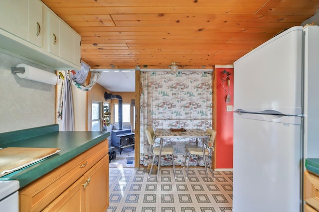 kitchen featuring wood ceiling, a wood stove, freestanding refrigerator, and white cabinets