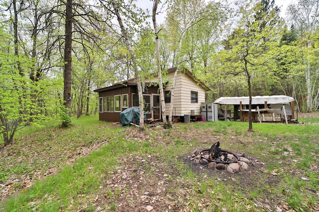 back of house with a fire pit, an outdoor structure, a wooded view, and a sunroom