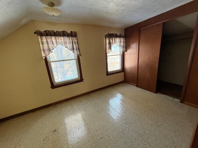 unfurnished bedroom with light floors, a closet, vaulted ceiling, a textured ceiling, and baseboards