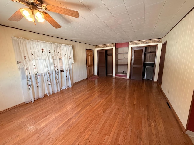 spare room with built in features, wood-type flooring, baseboards, and a ceiling fan