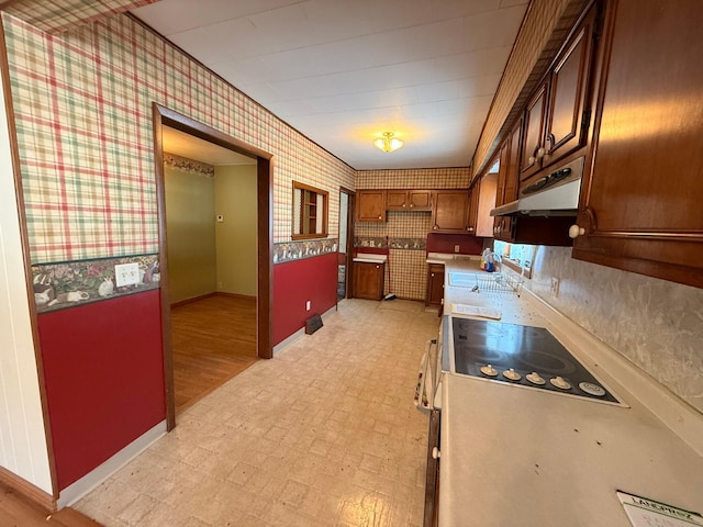 kitchen with under cabinet range hood, a sink, light countertops, light floors, and wallpapered walls