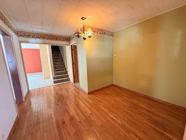 empty room featuring light wood-style flooring, stairway, baseboards, and an inviting chandelier