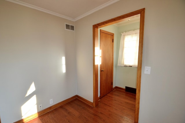 hallway featuring visible vents, ornamental molding, baseboards, and wood finished floors