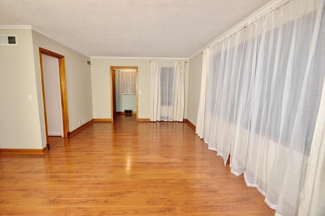 empty room with visible vents, baseboards, ornamental molding, light wood-style flooring, and a textured ceiling