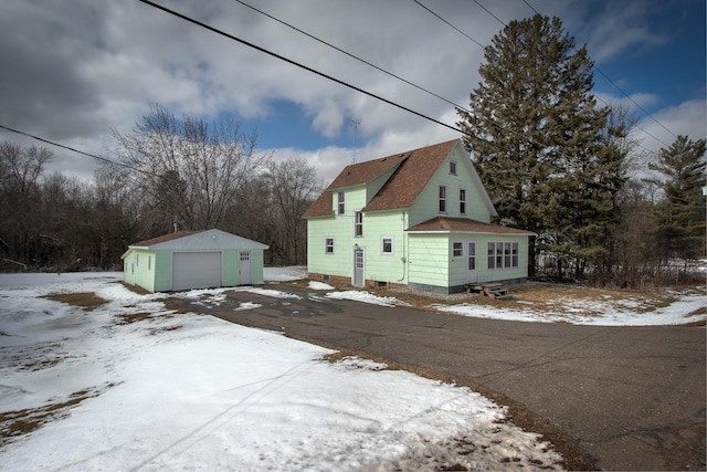 snow covered property with aphalt driveway, an outdoor structure, and a detached garage