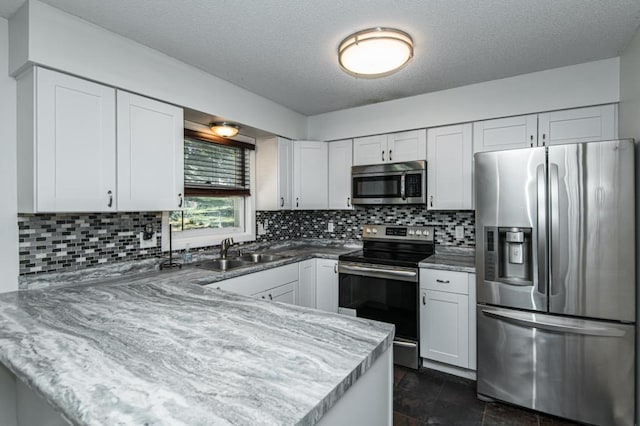 kitchen featuring appliances with stainless steel finishes, white cabinetry, a peninsula, and a sink