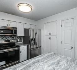 kitchen with backsplash, white cabinetry, and stainless steel appliances