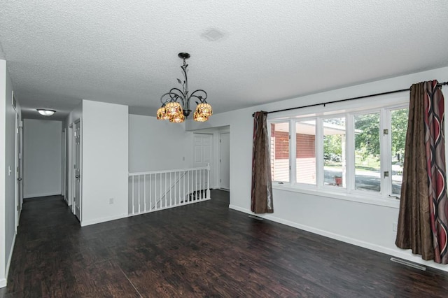 spare room with visible vents, a textured ceiling, dark wood finished floors, an inviting chandelier, and baseboards