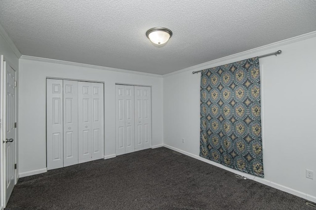 unfurnished bedroom featuring crown molding, multiple closets, dark carpet, and a textured ceiling