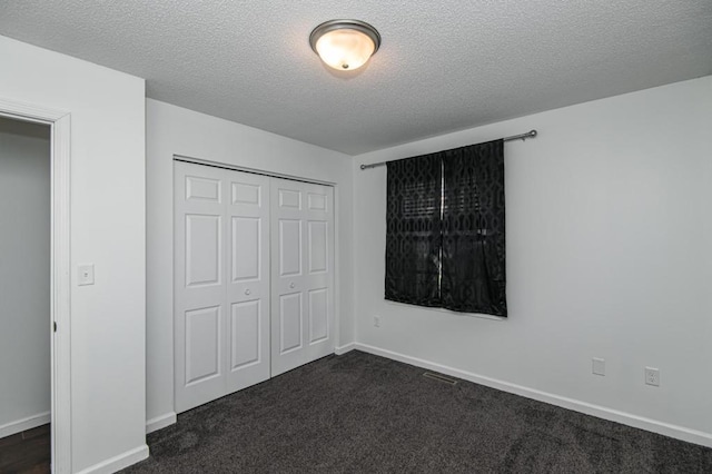 unfurnished bedroom with a closet, a textured ceiling, baseboards, and dark colored carpet